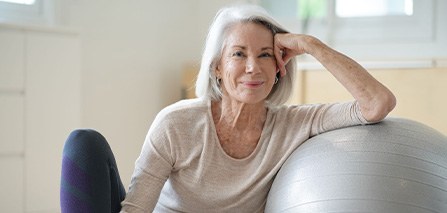 Senior woman smiling while resting against balance ball