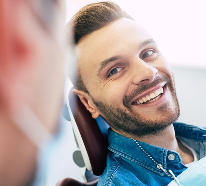 Man in denim shirt in dental chair smiling at dentist