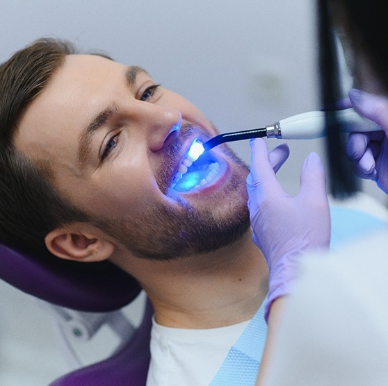 Dentist applying UV light to man’s dental bonding