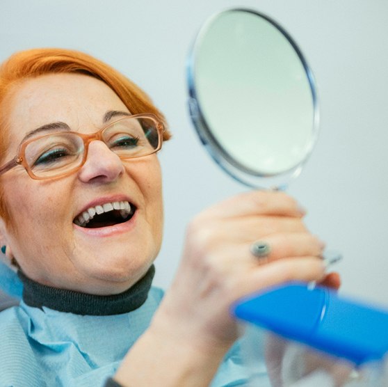 A woman admiring her dentures with a hand mirror