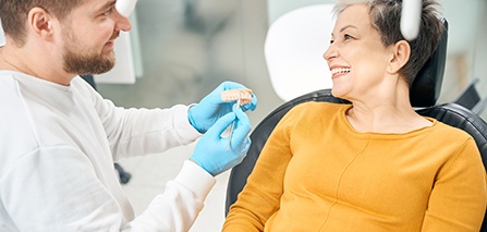 Smiling dentist showing patient model of denture