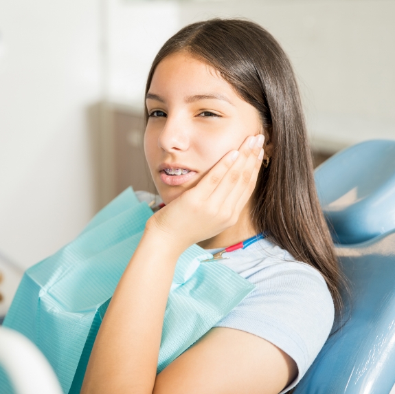 Teenage girl in dental chair holding her cheek in pain
