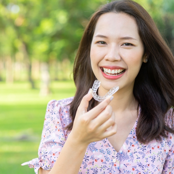 Woman smiling and holding an Invisalign tray outdoors