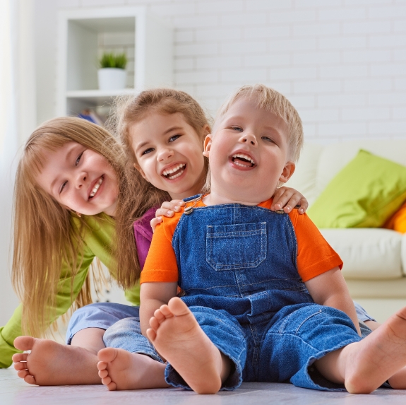 Three laughing children sitting on living room floor
