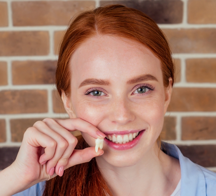 Smiling woman holding a tooth after tooth extractions in Putnam