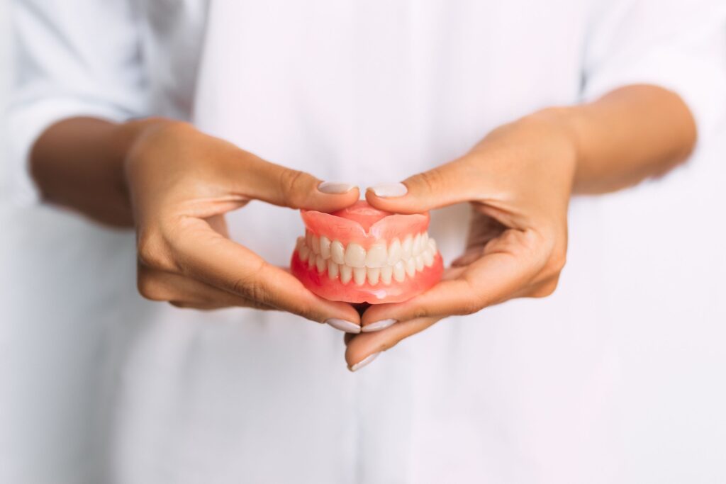 Woman with manicured nails holding dentures in front of abdomen 