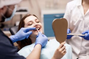 Dentist holding a shade guide sample to patient's teeth as she looks into mirror