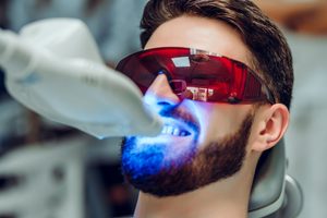 Man in dental chair with goggles with UV light on teeth during whitening